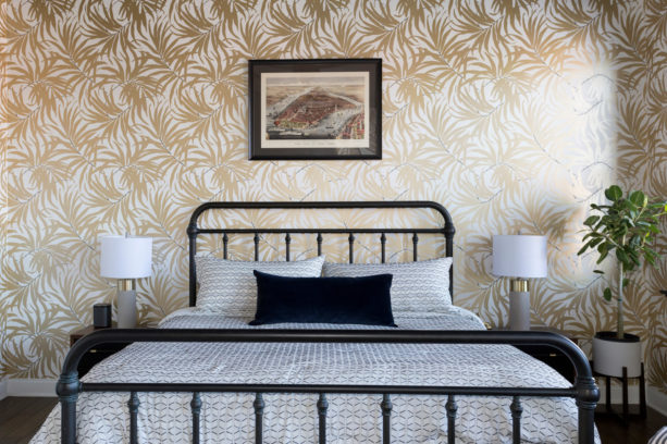 a black contemporary metal bed placed in front of a gold leaves accent wall