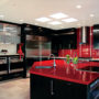 the combination between black cabinets and island with glossy red countertops and tiled backsplash