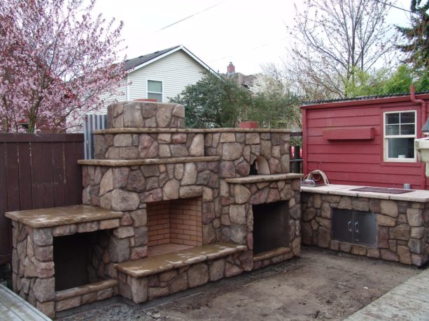 custom built outdoor fireplace with raised hearth, a pair of wood boxes, and pizza oven
