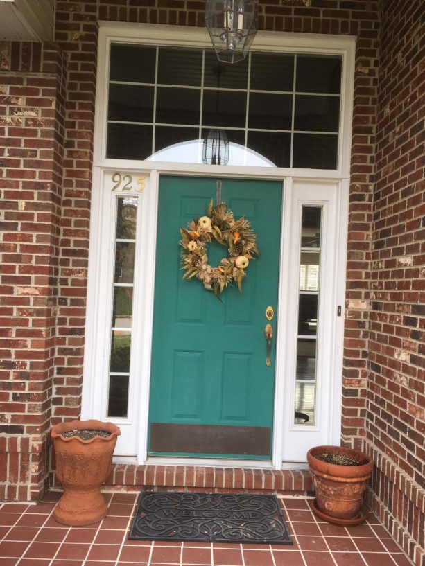 classic entry front door in teal surrounded by brick walls