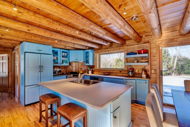 light blue cabinetry with gray countertops surrounded by wood elements in a log cabin kitchen