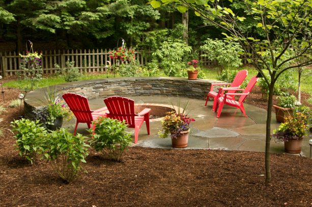 sunken fire pit with brick edging in a rustic landscape with red chairs as an accent
