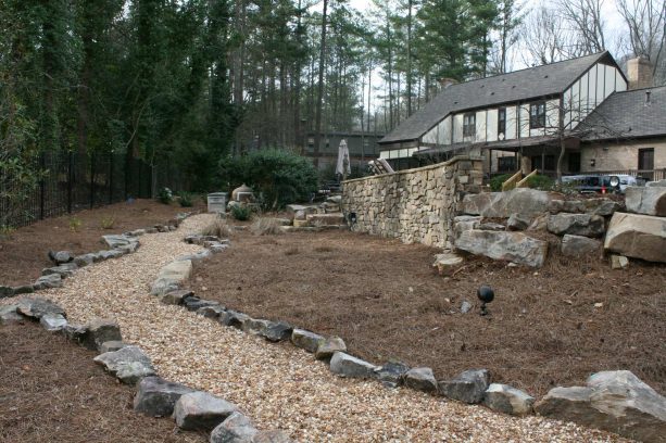 backyard rock garden with stone-lined pebble path and stone veneer wall