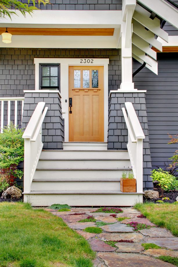 white window and exterior door trim with an overhang in a grey siding of a craftsman house