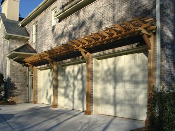 wooden pergola is attached to a brick wall over garage doors